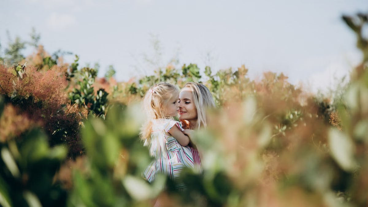 A touching moment between a mother and daughter surrounded by lush greenery outdoors.